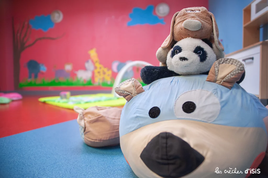 Coussin en forme d’animal dans une salle colorée de la crèche Jardin d’Isis à Illkirch, avec le panda Yoda et un chien en peluche empilés dessus, illustrant un moment de tendresse et de jeu dans un environnement sécurisé et bienveillant.